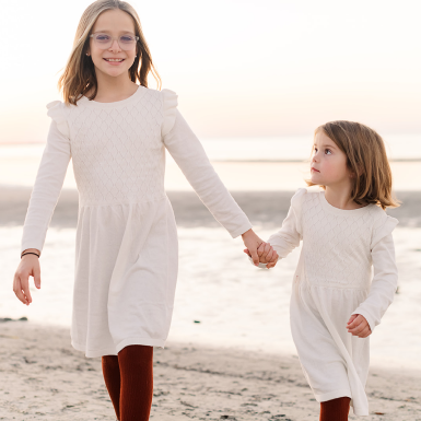 Kacey Carnegie's two daughters wearing white dresses hold hands on a beach
